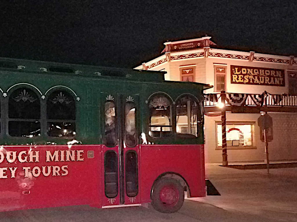 Red and green trolley at night passing in front of the illuminated Longhorn Restaurant in a historic western-style building.