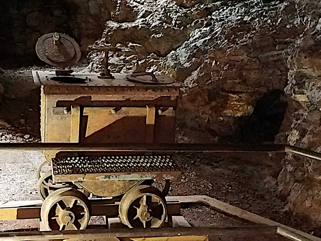 Rusty mining cart on rails inside an underground mine, surrounded by rocky walls and dim lighting.