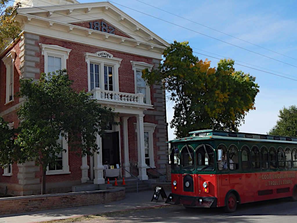 Historic brick courthouse with 'Cochise County' sign and construction date '1882' above the entrance, alongside a red and green trolley labeled 'Good Enough Mine & Trolley Tours.'